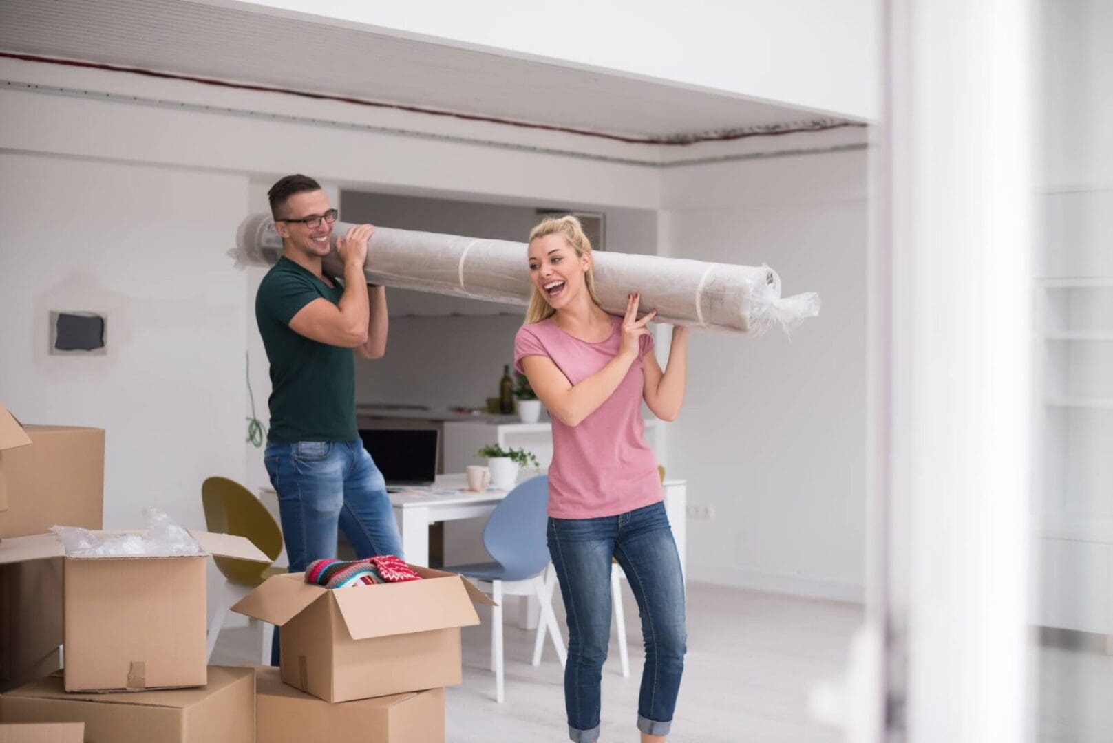 Young couple carrying a carpet moving in to new home together. Home, people, moving and real estate concept