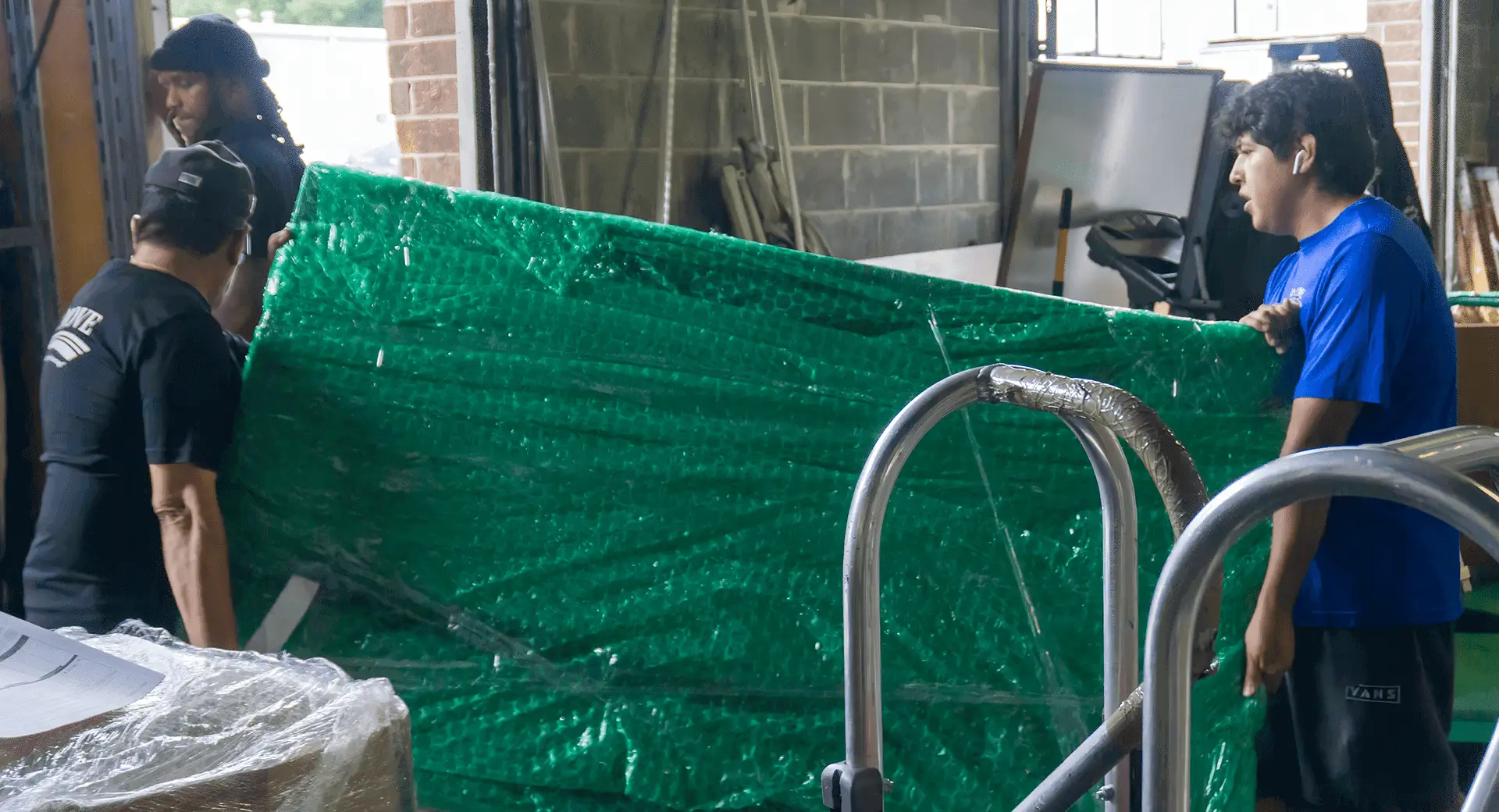Movers carrying a green-wrapped mattress.
